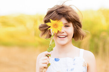 Obraz na płótnie Canvas Cute child girl wear dress with sunflower in summer field. Happy little girl hide eye with sunflower. Summer time concept.