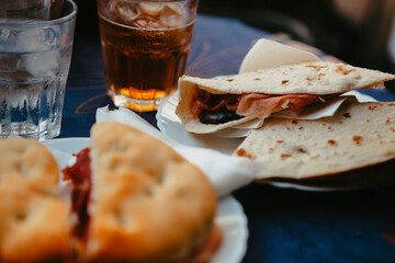 Traditional Italian food. Crispy panini and piadina sandwiches with prosciutto (speck), cheese, lettuce and vegetables with fresh drinks on a table with a blue tablecloth. Healthy European snack.