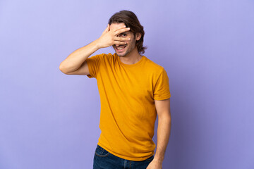 Young handsome man isolated on purple background covering eyes by hands and smiling