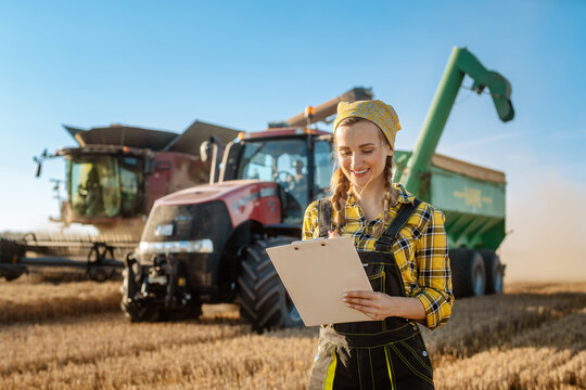 Farmer on grain field with tractor and combine harvester in background taking notes