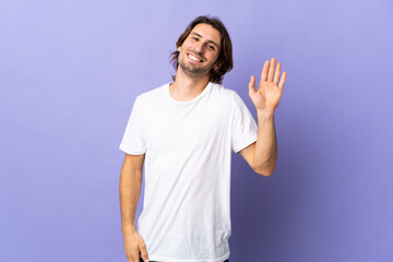 Fototapeta premium Young handsome man isolated on purple background saluting with hand with happy expression