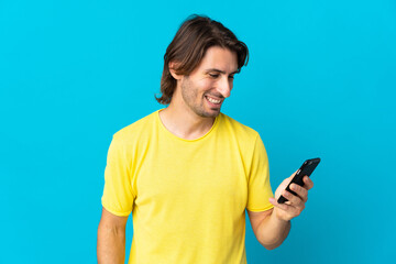 Young handsome man isolated on blue background sending a message or email with the mobile