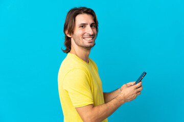 Young handsome man isolated on blue background sending a message or email with the mobile