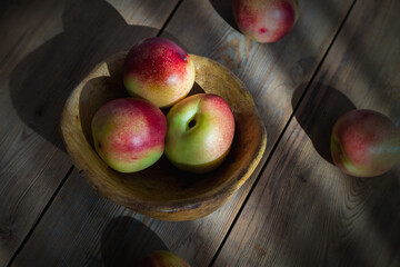 Red and green mini nectarine in a wooden bowl. The sun's rays illuminate the nectarine. Close-up.