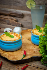 Pots with mushroom julienne on a wooden board, decorated with herbs. Julienne in cocotte with yellow cheese crust.