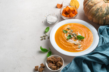 Pumpkin cream soup with pumpkin seeds and basil on a gray background. Side view.