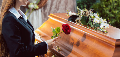 Mourning woman on funeral with red rose standing at casket or coffin