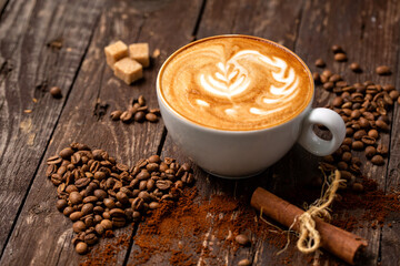 Latte espresso on a wooden table next to a pile of heart shaped coffee beans