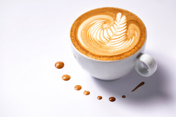 Cup of coffee with a rosette decoration surrounded by few brown drops on white background