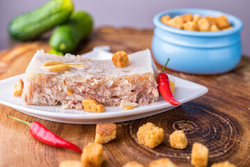 Beef and pork jellied meat on a white saucer. Cold appetizer with pieces of rusks and cucumber....