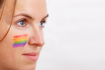 Portrait of a young woman with LGBT flag painted on her cheek. Theme of equality and freedom of choice