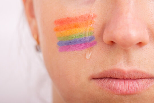 Part of the face of a young crying woman with a painted LGBT flag on her cheek. The concept of infringement of the rights and equality of LGBT people