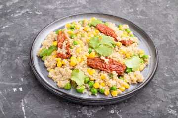 Quinoa porridge with green pea, corn and dried tomatoes on ceramic plate on a gray concrete background. Side view.