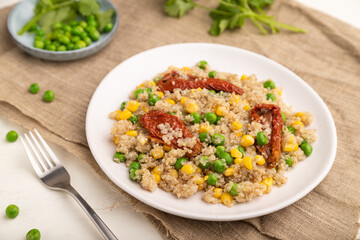 Quinoa porridge with green pea, corn and dried tomatoes on ceramic plate on a white wooden background. Side view, selective focus.