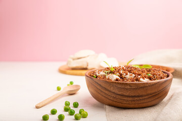 Quinoa porridge with green pea and chicken in wooden bowl on a white and pink background. Side view, selective focus, copy space.