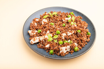 Quinoa porridge with green pea and chicken on ceramic plate on a pastel orange background. Side view.