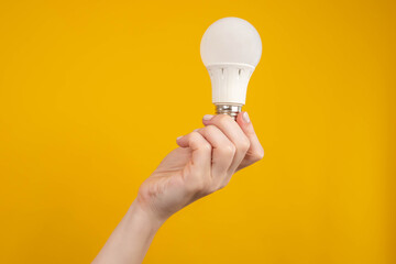 LED light bulb. Frosted white light bulb in hand. Concept - sale of LED lamps. LED light bulb on an orange background. It symbolizes electric diode lighting. Room lighting equipment.