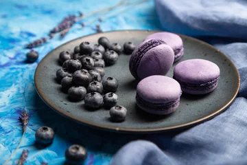 Purple macarons or macaroons cakes with blueberries on ceramic plate on a blue concrete background. Side view, selective focus. © zgurski1980