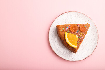 A piece of orange cake on a pastel pink background. Top view, copy space.