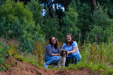 Naklejka na ściany i meble Lesbian couple and their dog pose for a photo in the woods. 