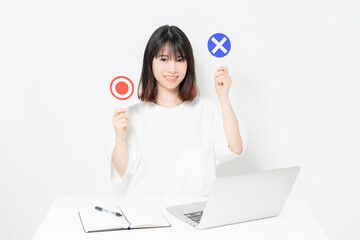 白背景の前でノートパソコンを使いながら、OKとNGのプラカードを持っている、若い女性