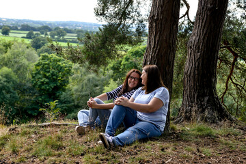 Lesbian couple lean against a tree chatting happily.