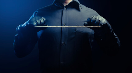 Photo of a shaded strangler assassin man in black shirt and leather gloves holding rope. - obrazy, fototapety, plakaty