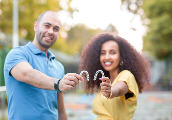 Happy and smiling couple from different races are holding an invisaligner. Includes copy and text...