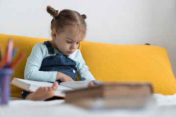 Naklejka premium Two preshool, toddler children read large interesting book of fairy tales on yellow bed. Siblings little twins reader have fun, happy kid on quarantine at home. Friendship, family, education concept