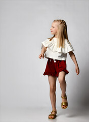 cute smiling little girl in a white blouse with flounces, burgundy shorts and sandals, walks briskly and looks to the side