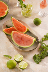 Watermelon slices, lime and mint in the morning light on sand-colored surface