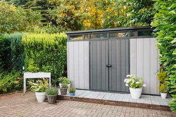 New garden shed in summer. Lots of pots of flowers next to a plastic garden shed. Relax in the...