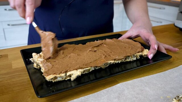 The cook spreads chocolate cream on the bottom level of the meringue cake. The process of making a chocolate tort with nuts and cream. cooking at home.