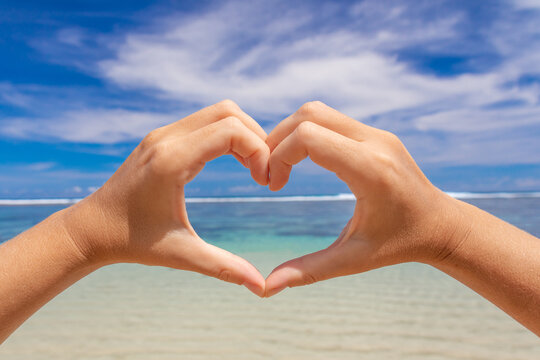 Women's hands in the shape of a heart on a background of blue sea and sky. Love concept.