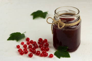 Red currant jam in a glass jar on light background