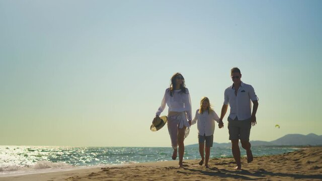 Backwards tracking of parents with son running on beach. People in summer clothing holding hands. Summer vacation at sea, relaxing on beach.