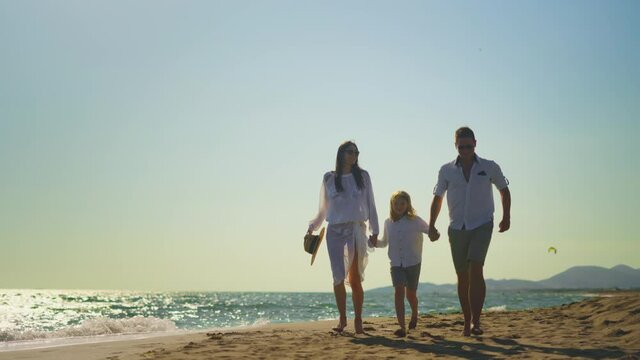 Backwards tracking of parents with son running on beach. People in summer clothing holding hands. Summer vacation at sea, relaxing on beach.