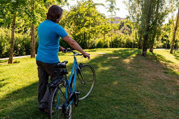 Unrecognizable man walking in the park with his bicycle