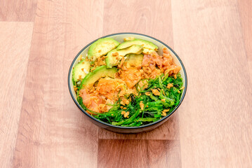 Hawaii salmon poke bowl with avocado, smoked salmon, crispy onion and wakame seaweed on wooden table