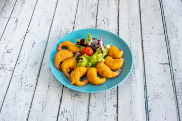 Portion of breaded and fried gabardine prawns with a simple salad of lettuce and cherry tomato as garnish