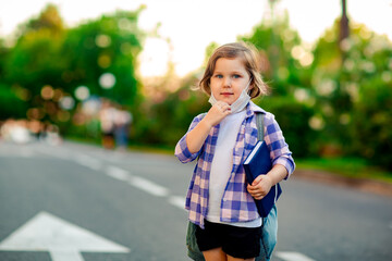 a schoolgirl is standing on the road in a plaid shirt and a medical mask, with a school backpack and a diary in her hands