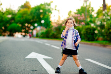 a schoolgirl is standing on the road in a plaid shirt and a medical mask, with a school backpack and a diary in her hands