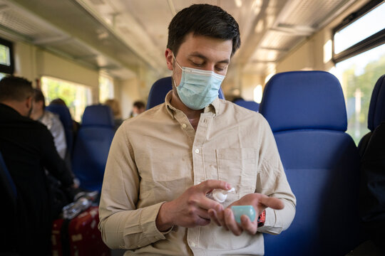 New Normal Commuting With Face Mask And Hand Sanitizer. Travel Safely On Public Transport. Passenger With Protective Mask Disinfects Hands In A Railway Train. Travel During Covid 19, Personal Protect