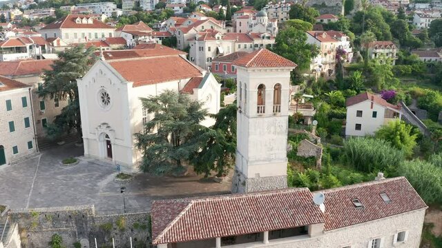 Bell tower and stone St Jerome church in the old medieval town in the Mediterranean. Historical Catholic Christian cathedral on the sloping hill in Herceg Novi, Montenegro, Europe. Aerial drone view.