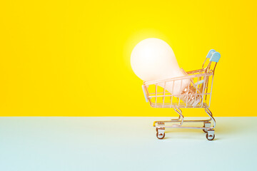 Light bulb in the toy Shopping cart or trolley on bright yellow background. Electricity sale or eco...