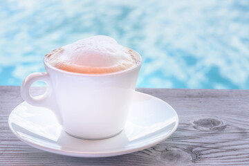 Foam on cappuccino in white cup against blurred water background