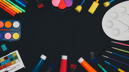 School art supplies on black.
Paints, pencils, brushes and markers are arranged in a frame on a black background with space for text in the middle, top view close-up.
