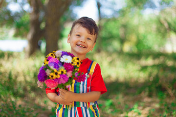 Smiling boy with a bouquet of wildflowers, a surprise for mom in the holiday. A child with flowers in bright clothes. red T-shirt in nature with a bouquet of chrysanthemums and daisies