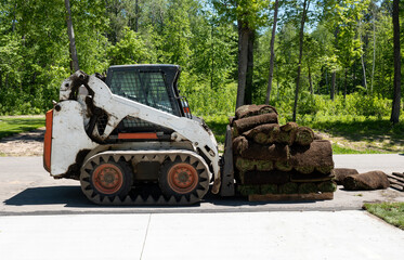 A compact front loader and a pallet with rolls of sod grass for installation at a new home...