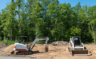 A mini excavator and compact front loader on dirt at home construction lot.